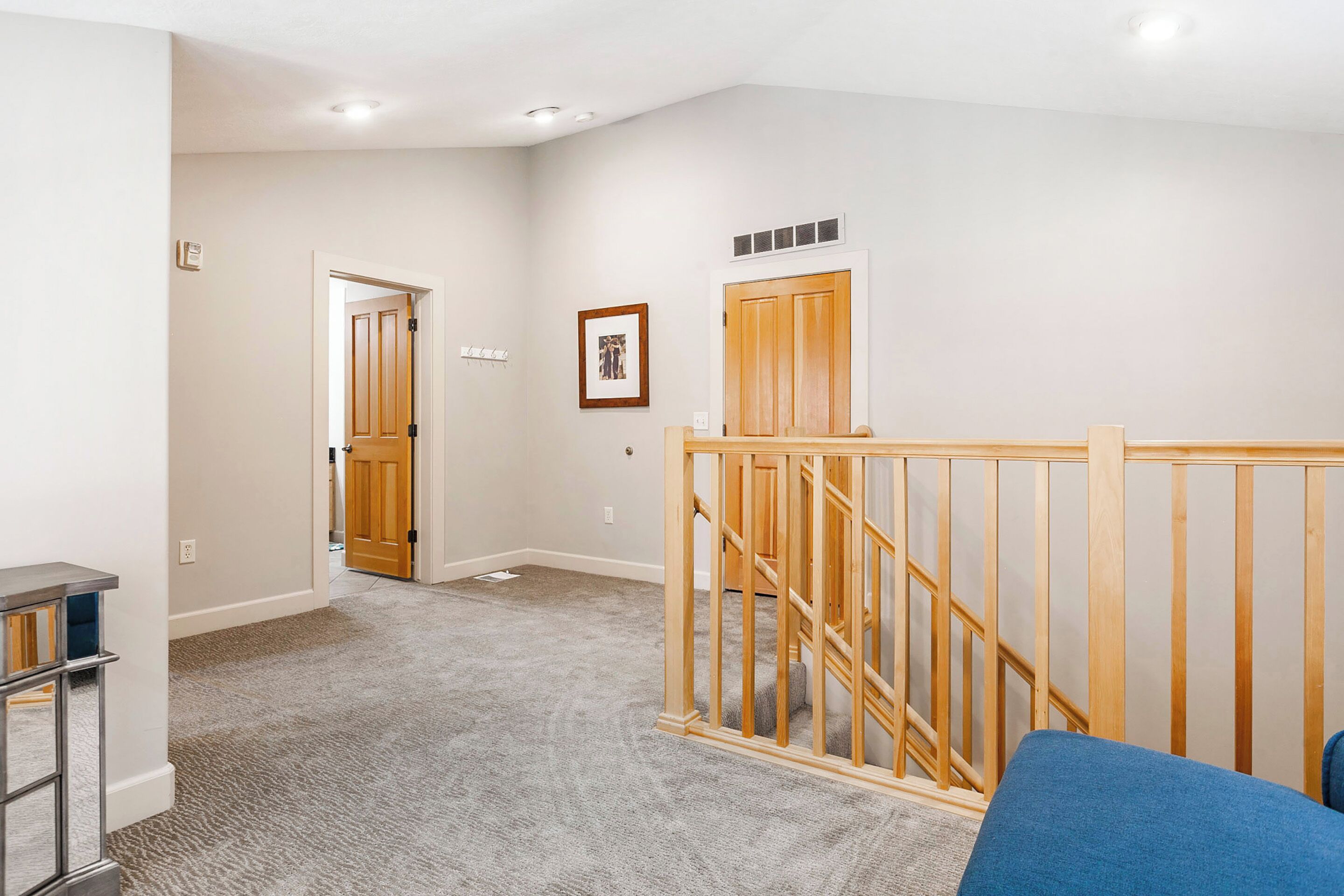 A hallway with a carpeted floor, a wooden railing, and a door leading to another room.