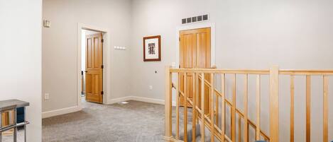 A hallway with a carpeted floor, a wooden railing, and a door leading to another room.