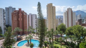 Un grand hôtel avec une piscine entourée de palmiers, et une montagne en toile de fond.
