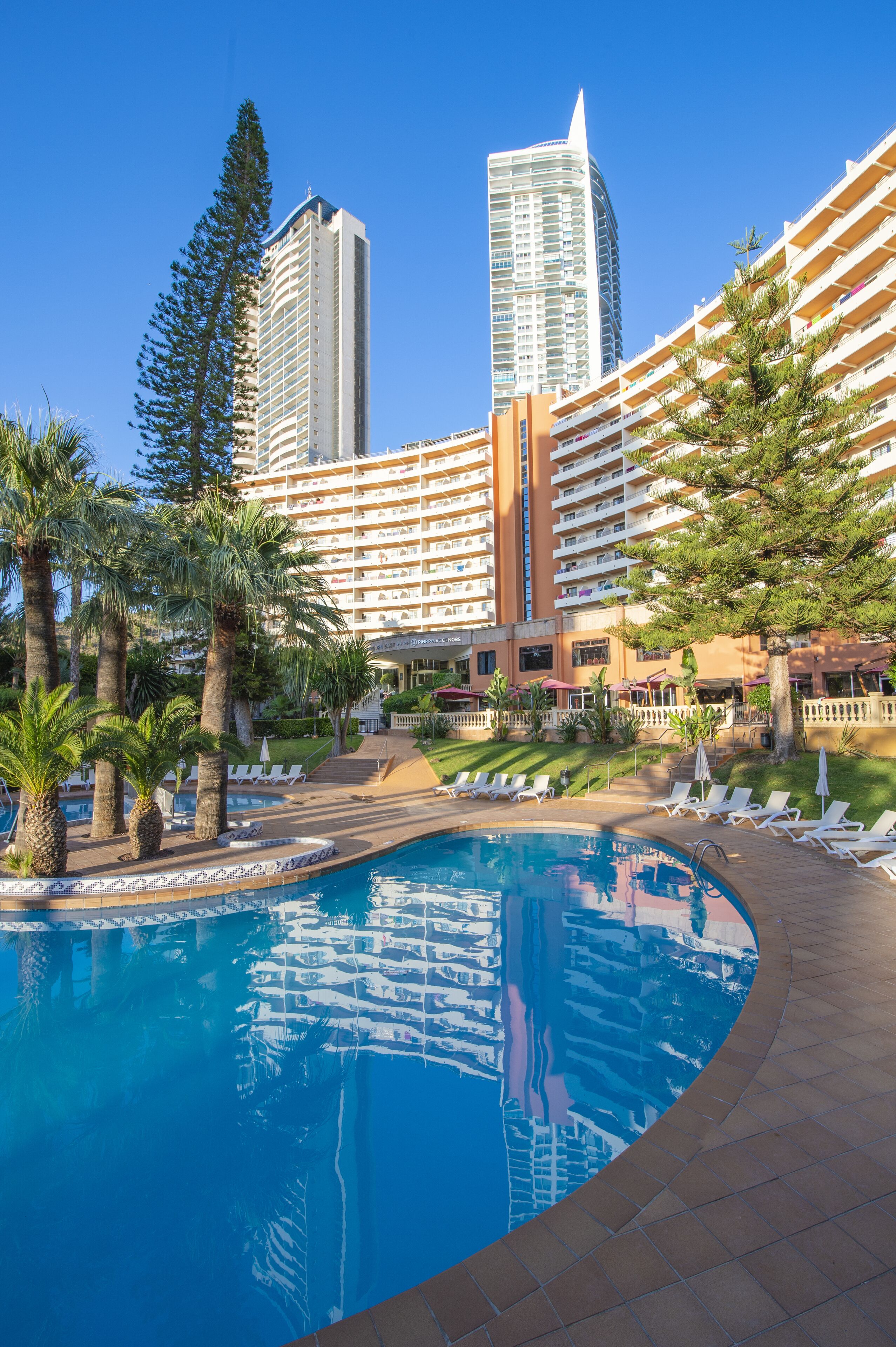 A hotel with a swimming pool, palm trees, and high-rise buildings in the background.