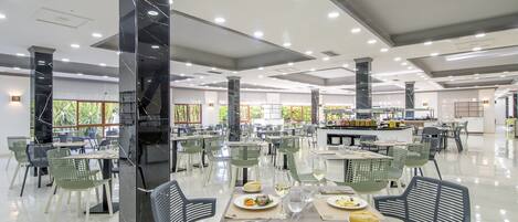 A spacious dining area with multiple tables and chairs, a central serving station, and a modern ceiling design.