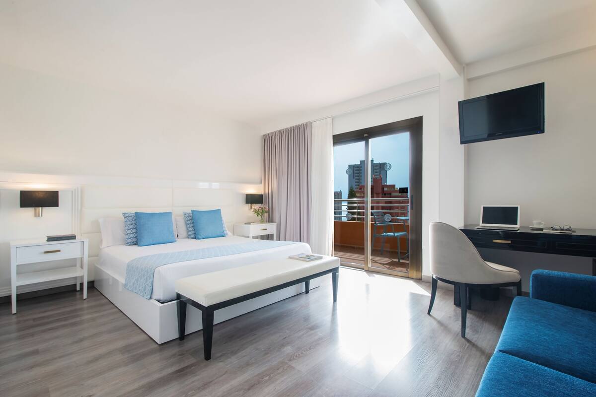 Une chambre d’hôtel moderne dotée d’un grand lit, d’un bureau, d’une chaise et d’un balcon offrant une vue sur la ville.