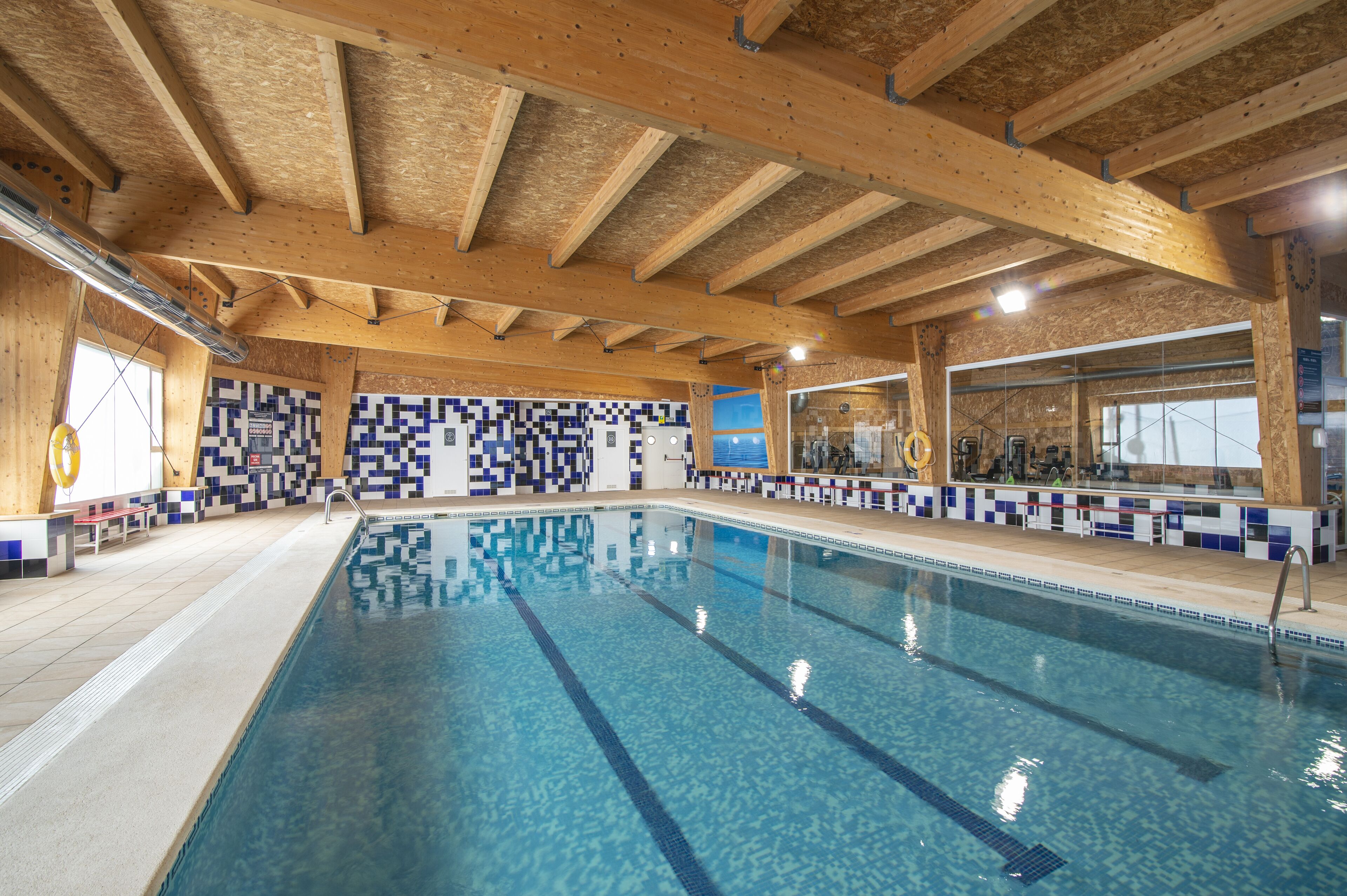 Una piscina interior con vigas de madera, paredes de azulejos y zona de baño despejada.