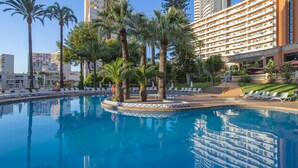 Un hôtel doté d’une piscine entourée de palmiers et de chaises longues.