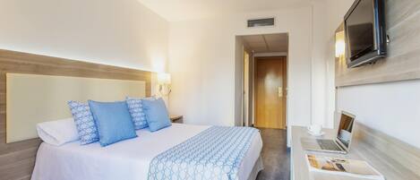 Una habitación de hotel con una cama, un escritorio con una computadora portátil y un televisor montado en la pared.