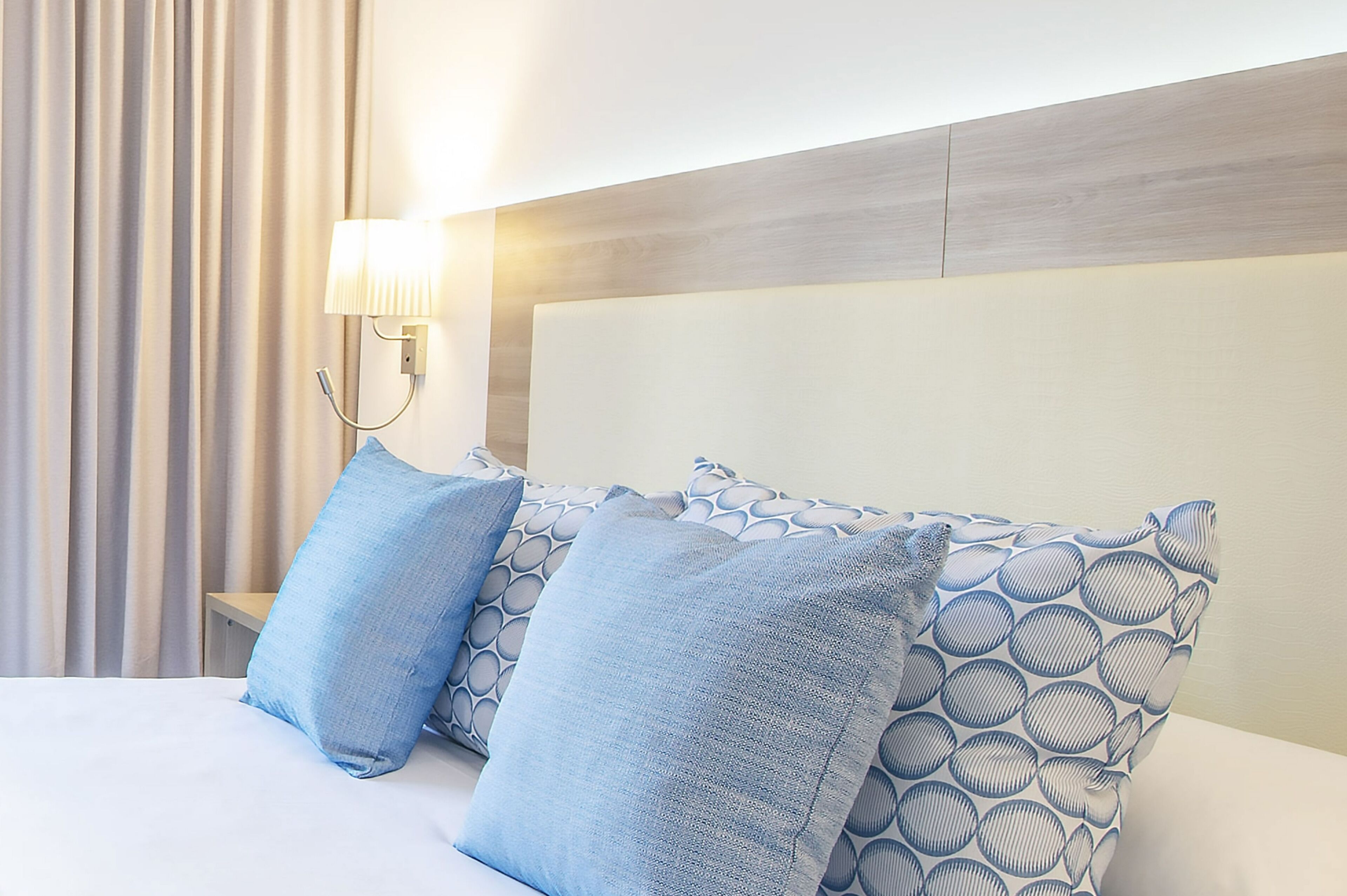 A neatly made bed with blue patterned pillows, a bedside lamp, and a wooden headboard.