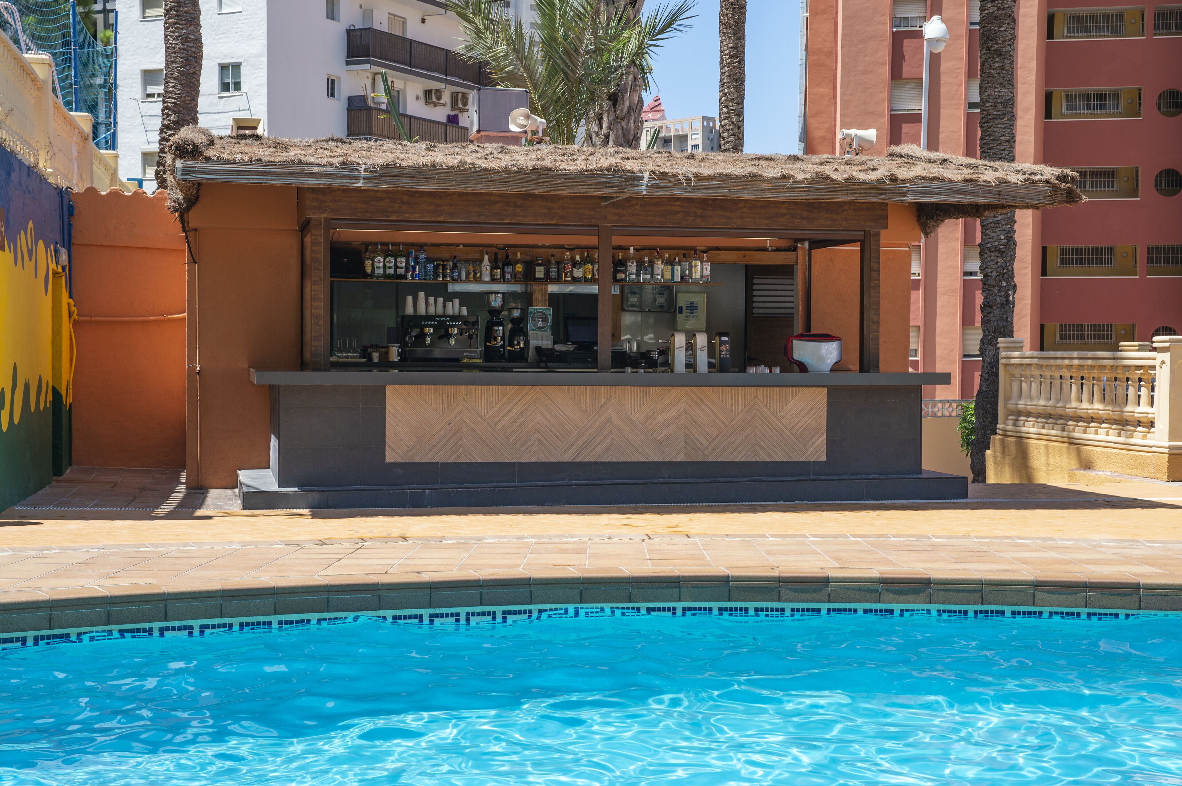 Um bar à beira da piscina, com balcão de madeira e prateleiras cheias de garrafas, próximo a uma piscina.