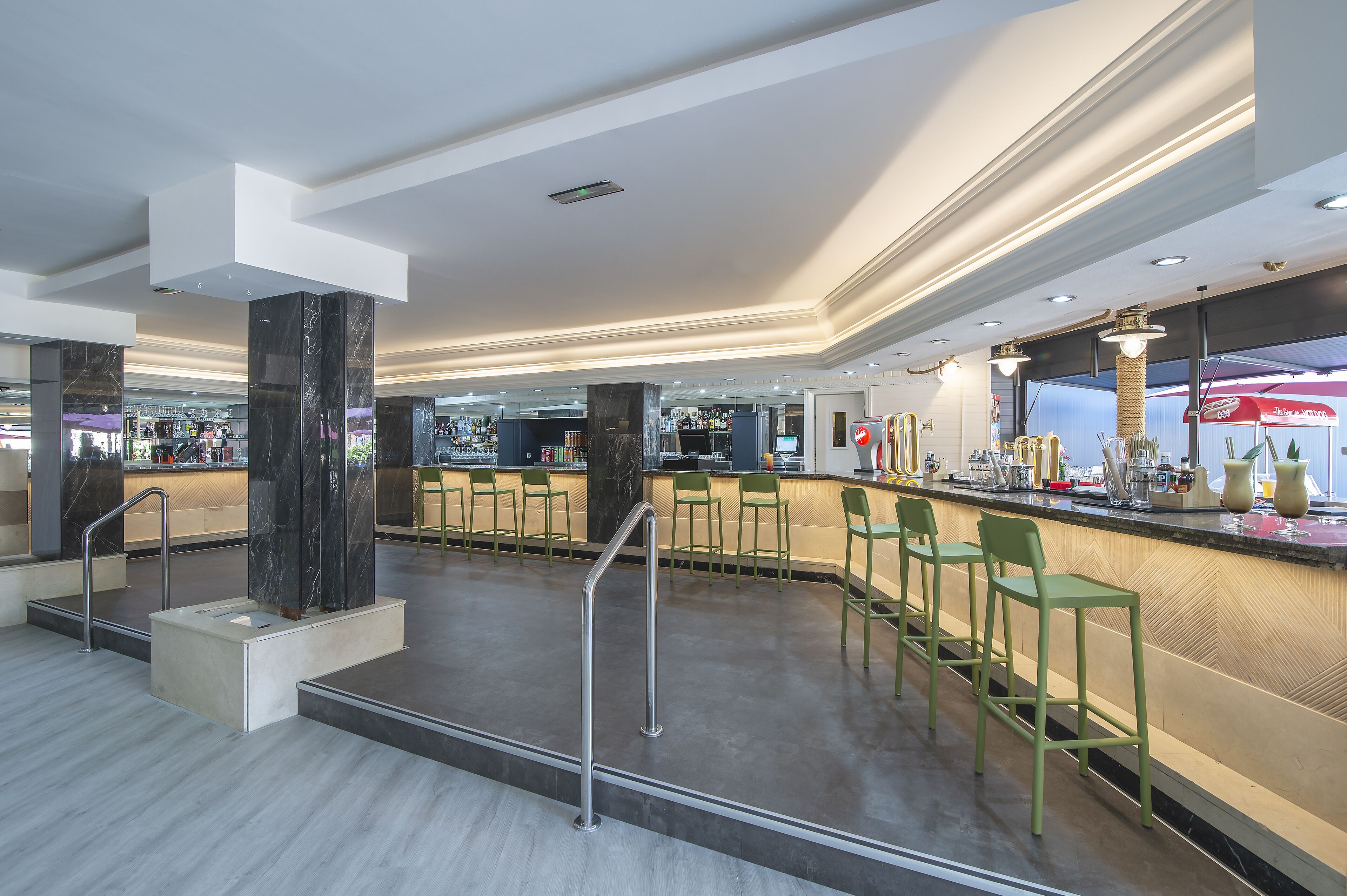 Eine moderne Bar mit einer Marmorsäule, grünen Barhocker und einer Theke mit verschiedenen Gegenständen.