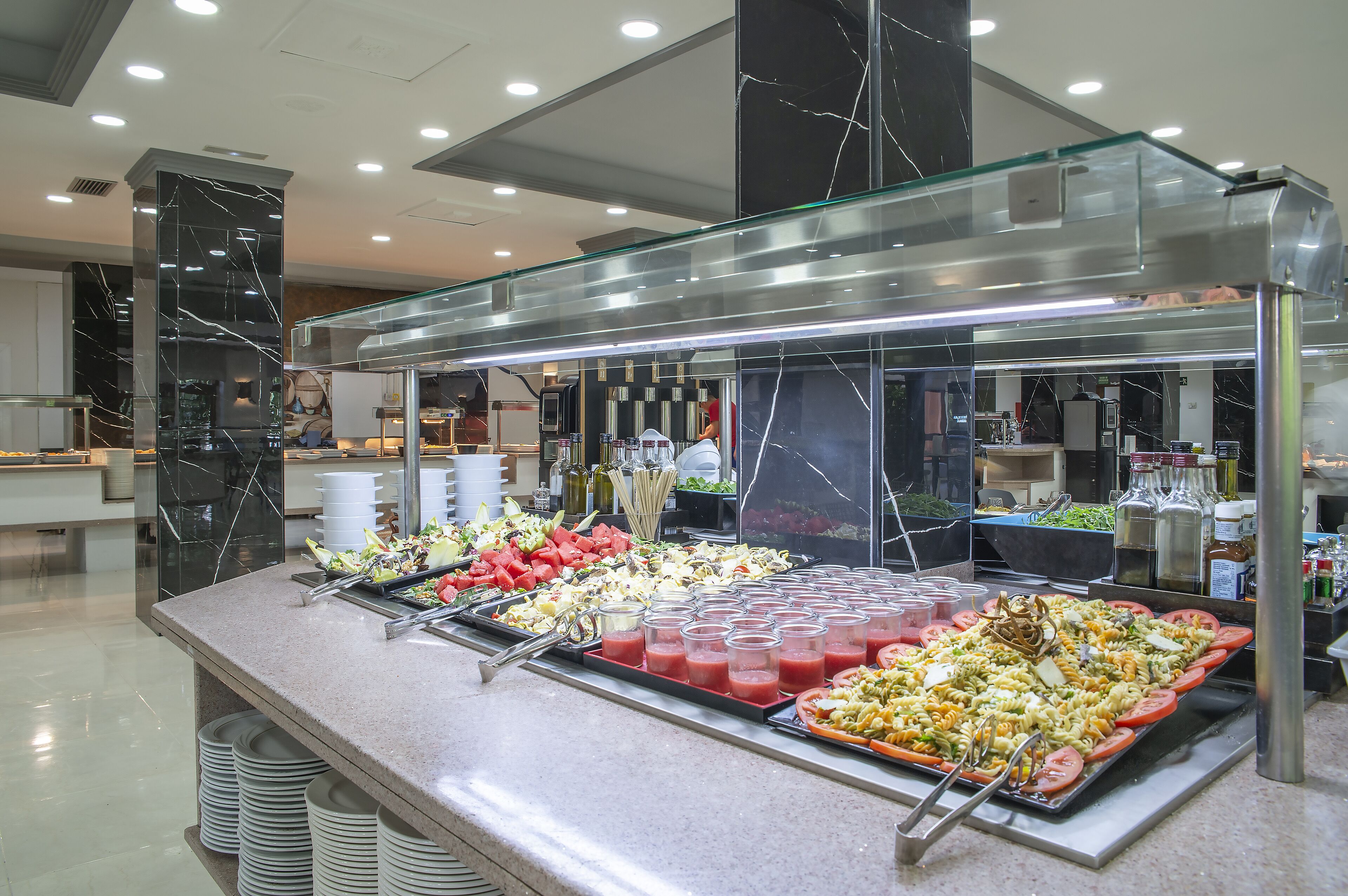 Ein Buffet mit verschiedenen Speisen und Getränken, eine Marmorsäule und eine Glaskonstruktion.