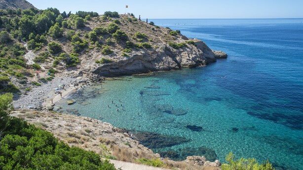 Un paysage côtier caractérisé par des eaux turquoise limpides, un terrain rocheux et une végétation clairsemée.