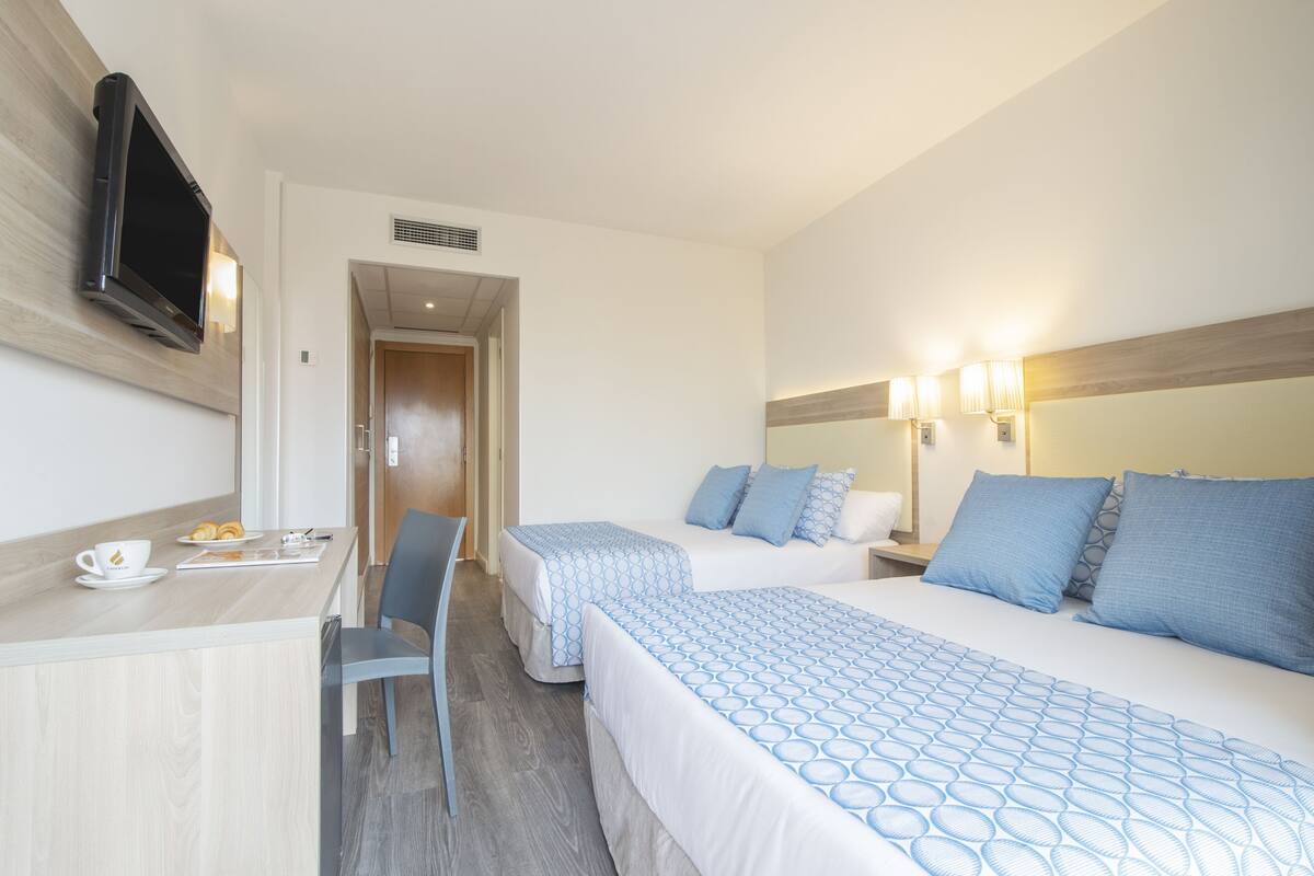 Une chambre d’hôtel avec deux lits, un bureau avec une tasse et des viennoiseries, et un téléviseur fixé au mur.