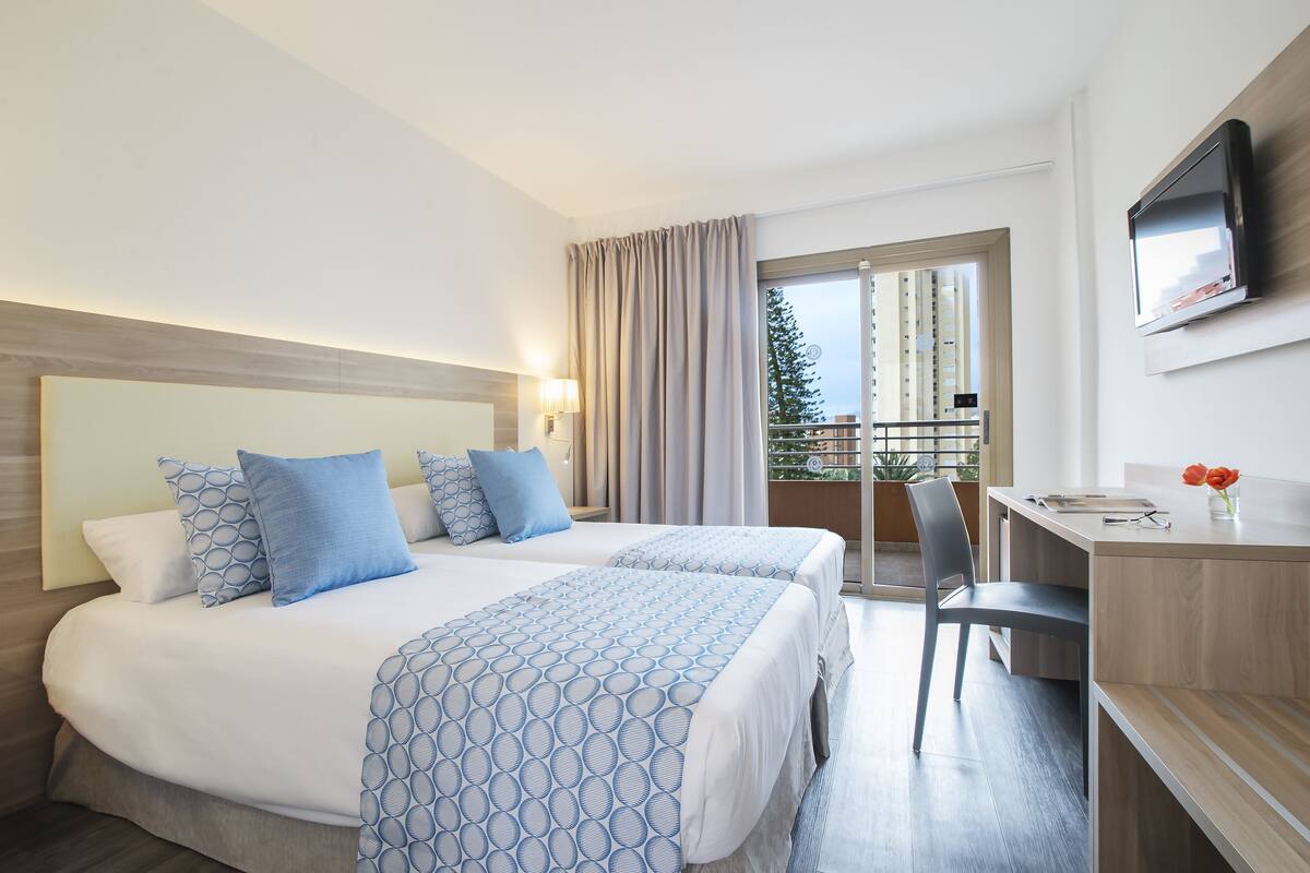 Une chambre d’hôtel avec deux lits, un bureau, une chaise, une télévision et un balcon avec vue.