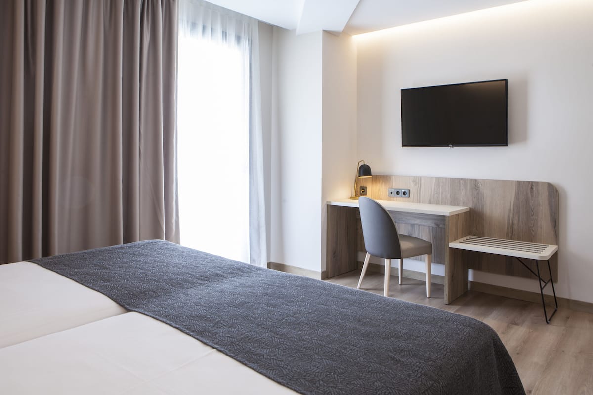A modern hotel room with a bed, desk, chair, and a flat-screen TV mounted on the wall.