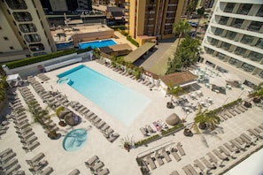 An aerial view of a hotel with a large swimming pool, sun loungers, and a small beach area.