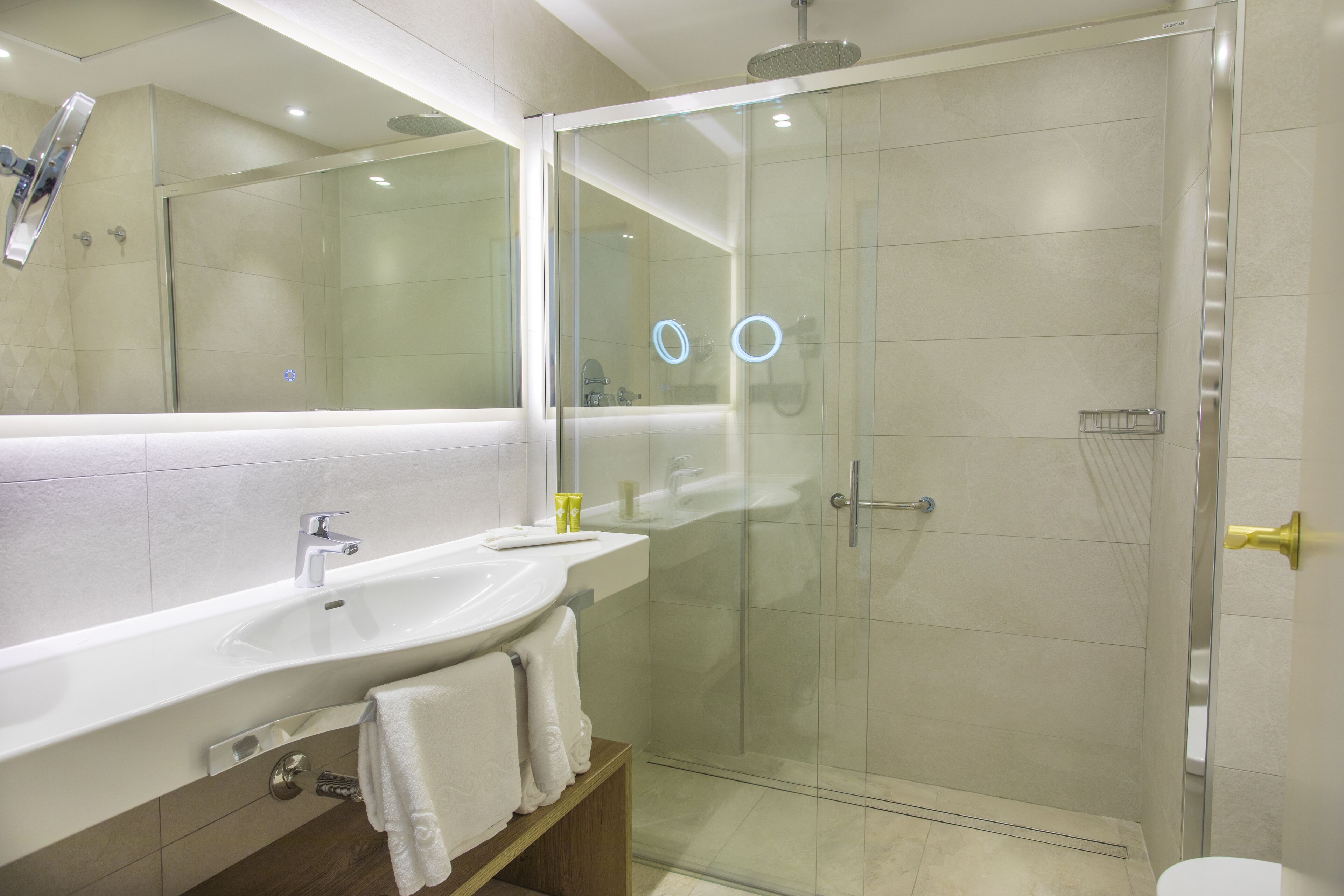A modern bathroom with a glass-enclosed shower, a large mirror, and a white sink.