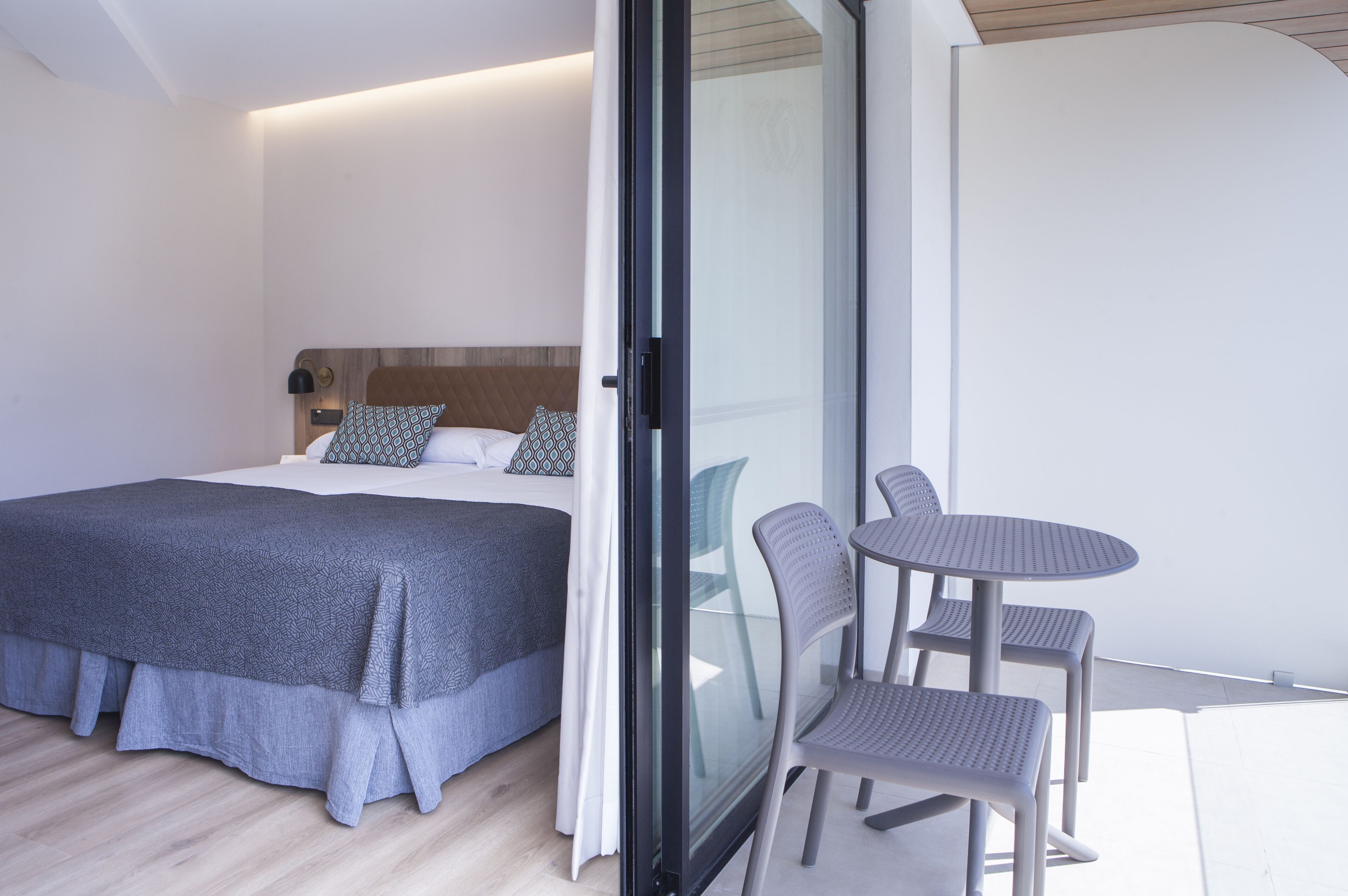 A bedroom with a bed, a glass door leading to a balcony, and a small table with chairs.