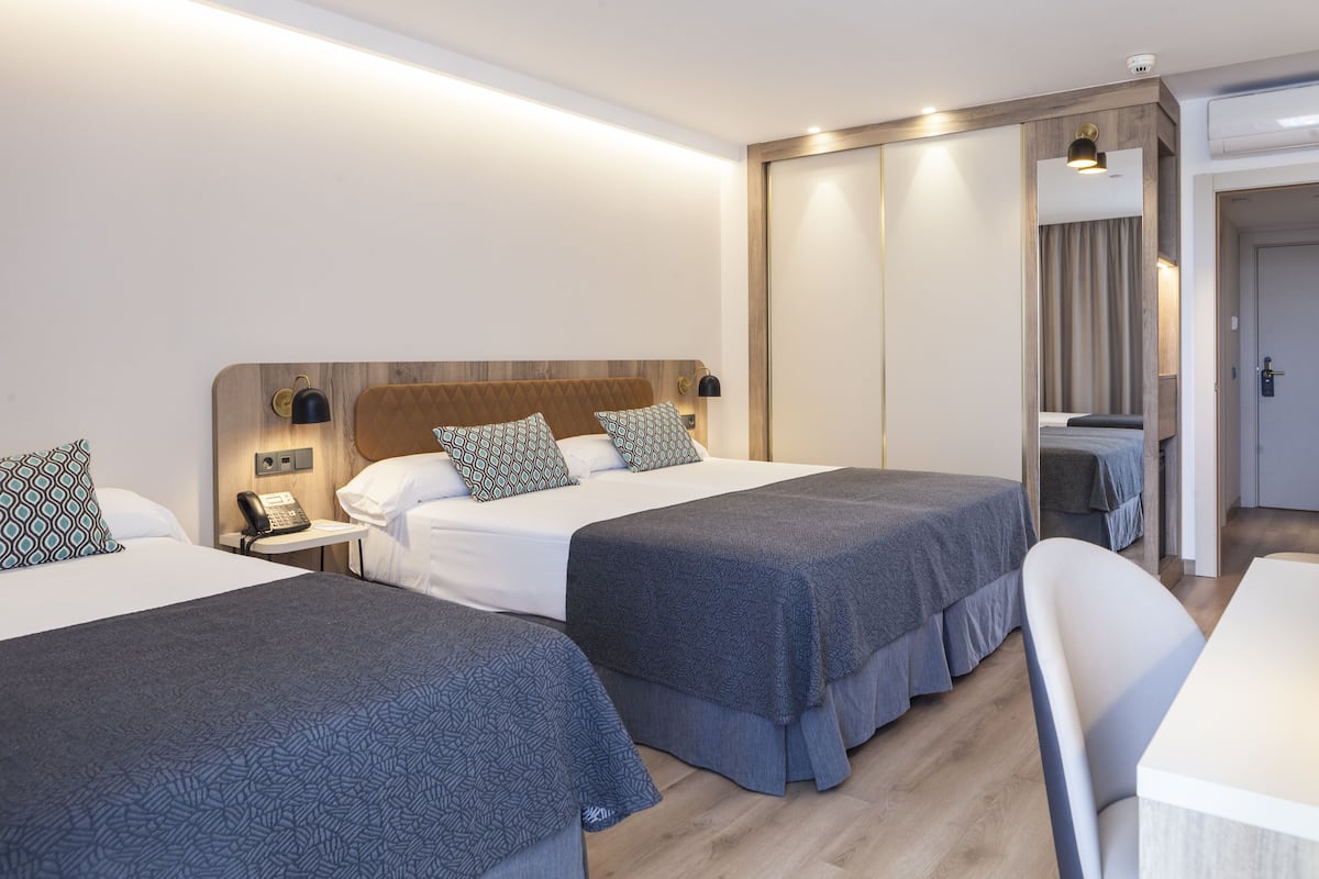 A hotel room with two beds, a desk, a chair, and a wardrobe.