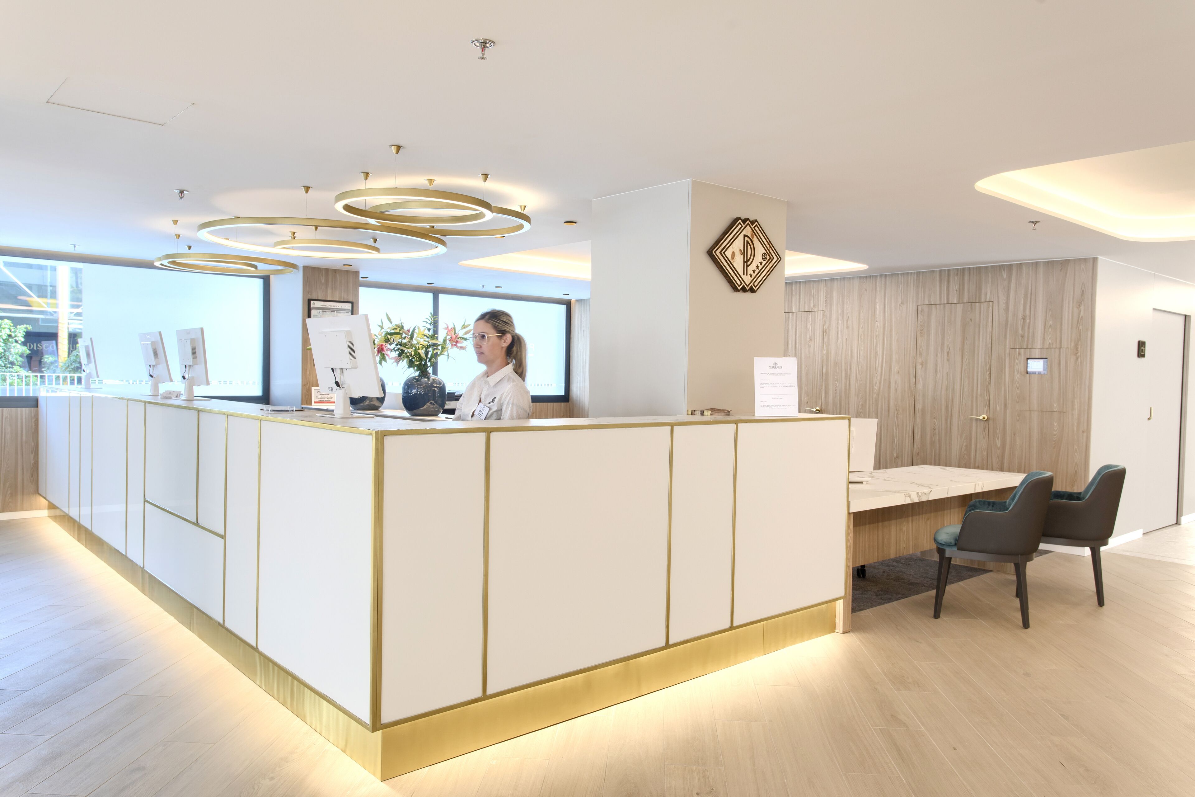 A reception area with a modern design, featuring a reception desk, a seating area with two chairs, and a large window providing natural light.