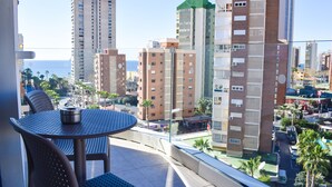 Un balcone con un tavolo rotondo e sedie, affacciato su una città con grattacieli e palme.
