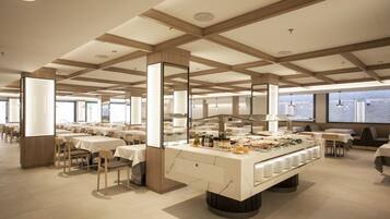 Uma sala de jantar moderna com buffet central, várias mesas e teto alto com vigas de madeira.