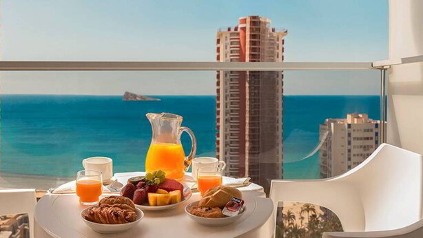 A breakfast table with fruit, pastries, and orange juice, overlooking a cityscape and the sea. - Don Pancho (Benidorm)