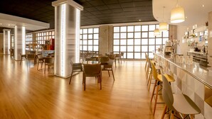 Un espacio interior amplio con piso de madera, una zona de bar con taburetes y mesas con sillas.