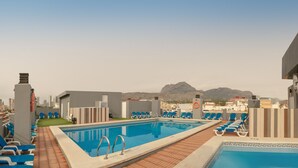 Piscina en la azotea con sillas reclinables azules, un flotador salvavidas y vistas a montañas.
