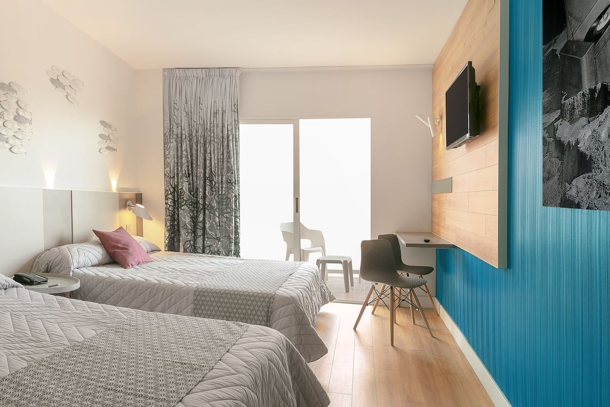 A modern hotel room with two beds, a desk, a chair, and a large window.