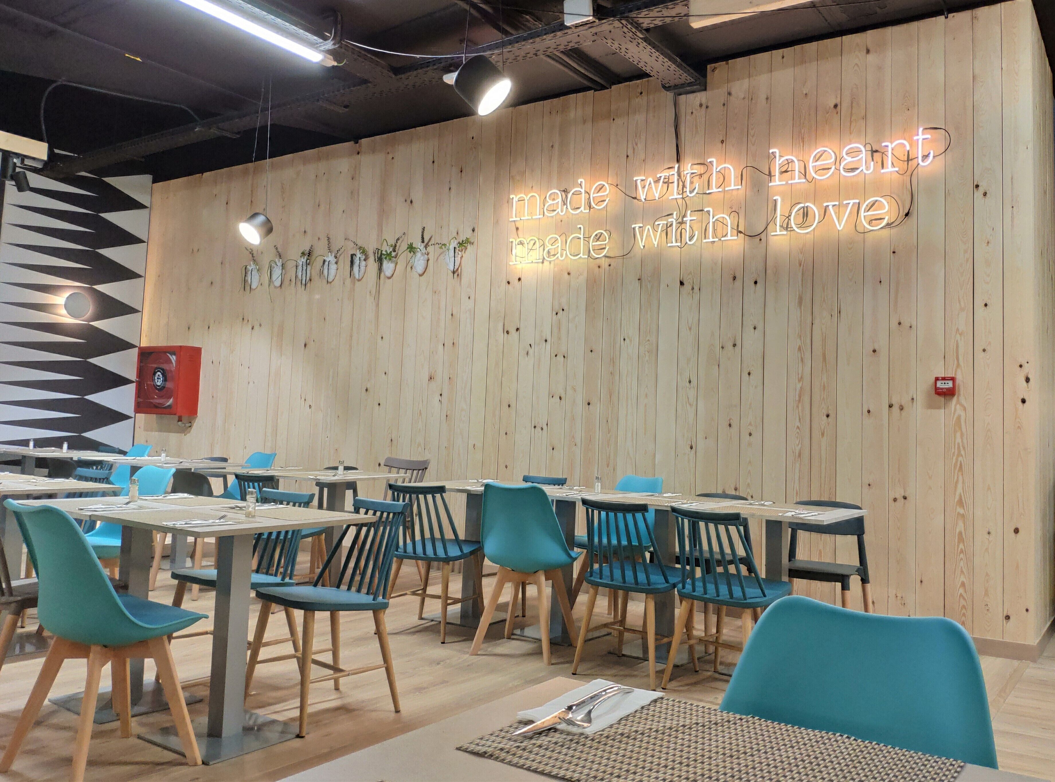 Interior de restaurante con paredes de madera, letreros de neón y sillas azules.