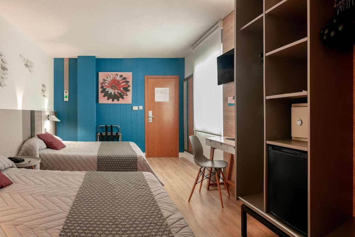 A modern bedroom with two beds, a desk, and a wardrobe.