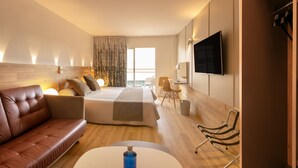 Una habitación de hotel moderna con un sofá de cuero, una cama con cabecera de madera, un televisor de pantalla plana y un escritorio con una silla.