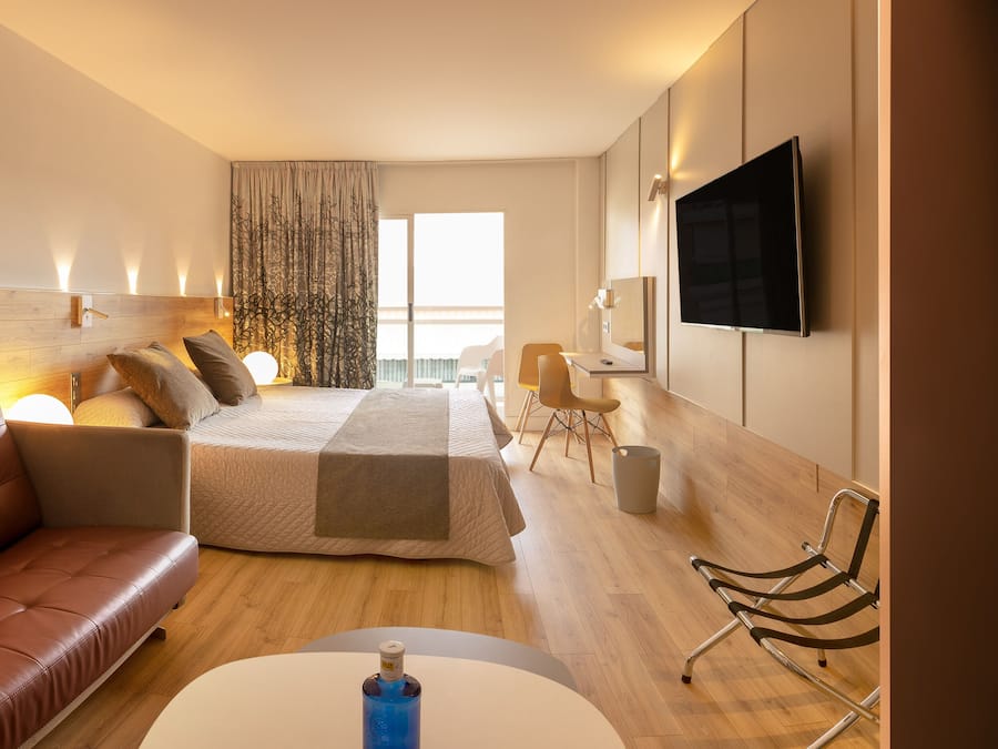 Una habitación de hotel moderna con un sofá de cuero, una cama con cabecera de madera, un televisor de pantalla plana y un escritorio con una silla.