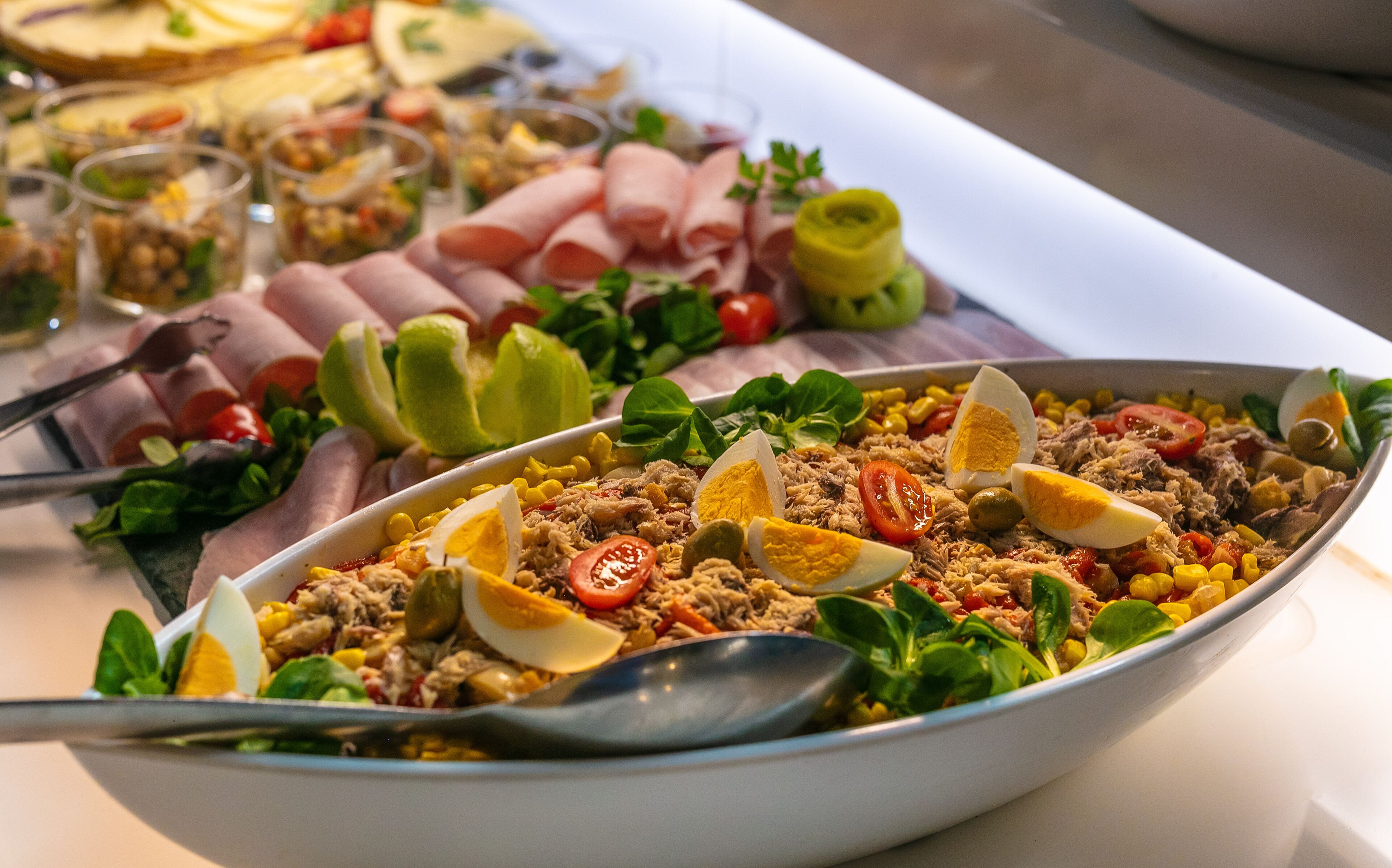 Un bufé con diversos platos, incluyendo una ensalada con huevos, maíz y tomates.