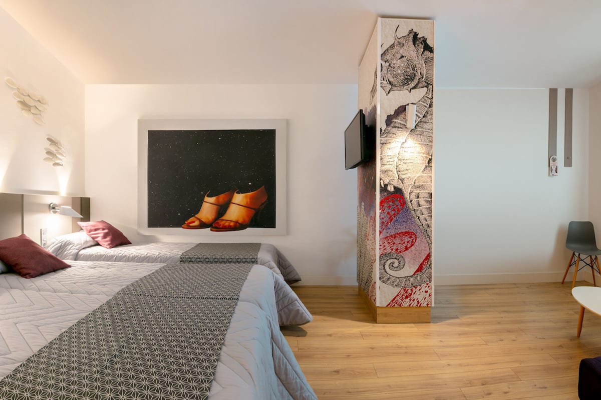 A modern hotel room with two beds, a desk, a chair, and a large artwork on the wall.