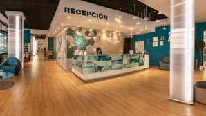 Zona de recepción con diseño moderno, que incluye un mostrador de recepción, área de estar con sofás y piso de madera.