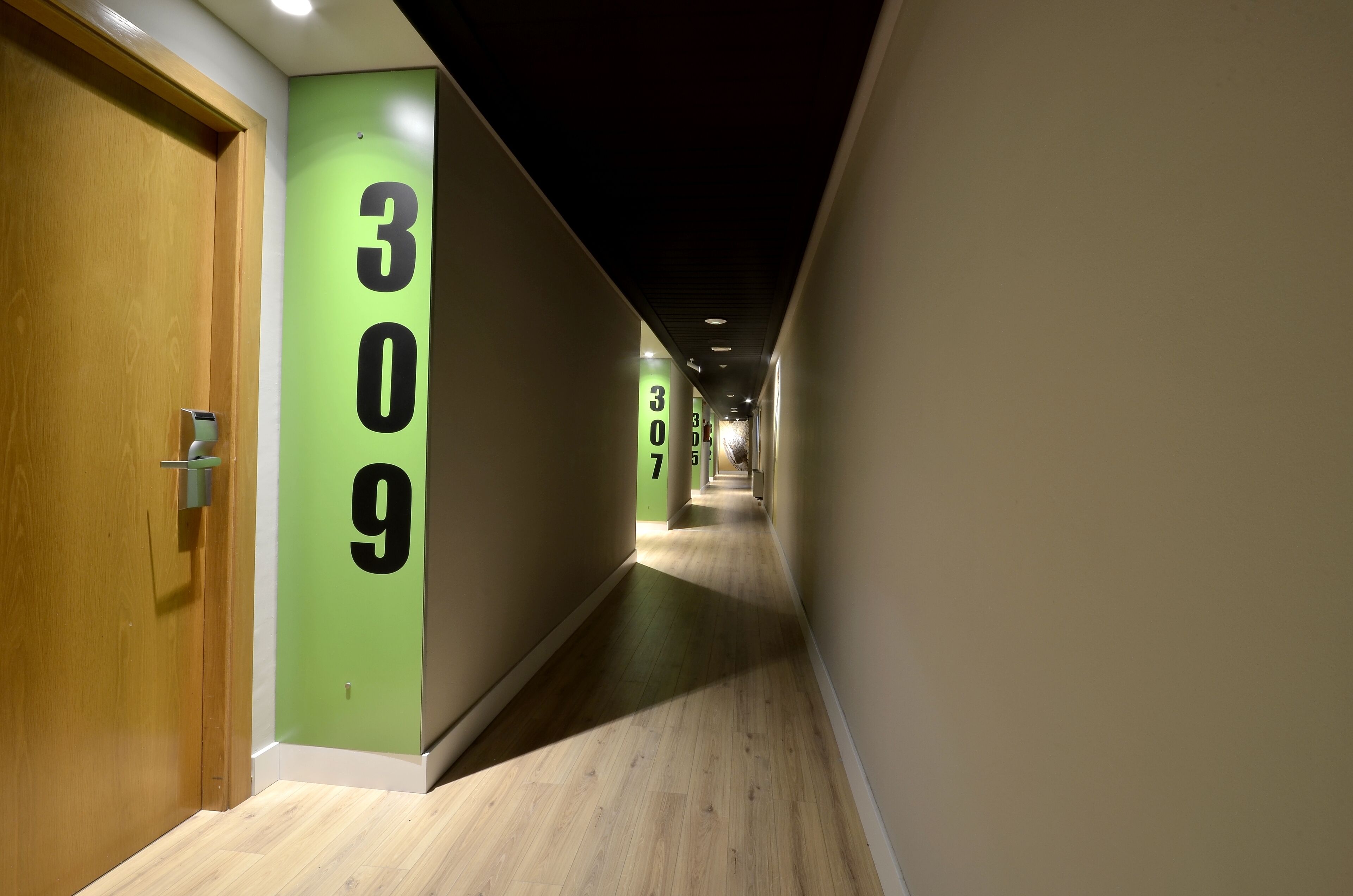 A hallway with green walls and wooden flooring, featuring numbers 309 and 307 on the walls.