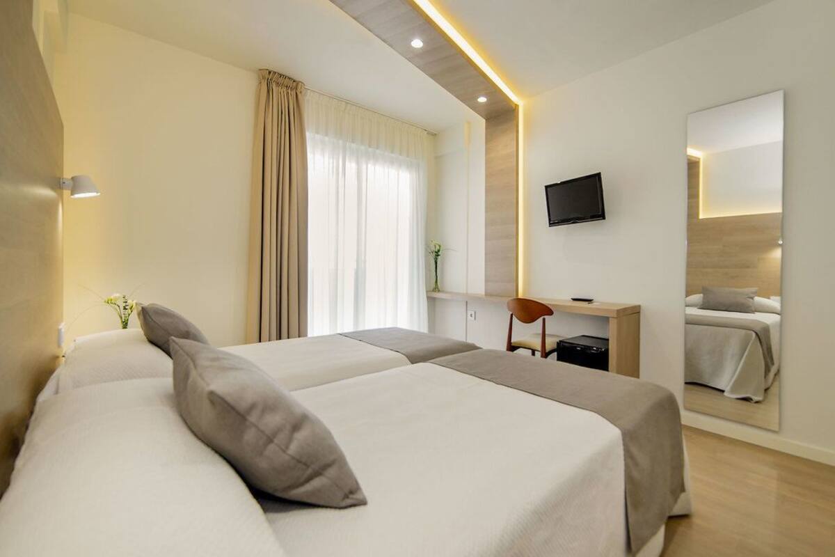 A hotel room with two beds, a desk, a chair, a TV, and a mirror.