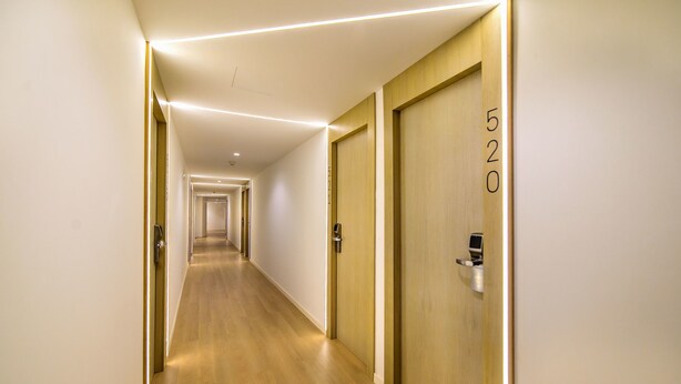 Pasillo de hotel con puertas de madera, cada una marcada con un número, y un interior moderno y bien iluminado.