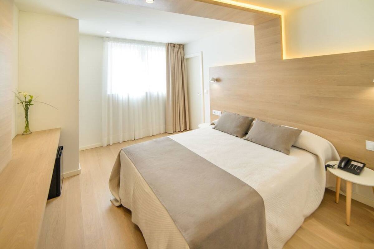 A modern hotel room with a large bed, a bedside table with a phone, and a window with curtains.