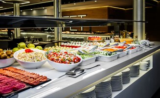Monipuolinen buffet, jossa on tarjolla erilaisia ruokia, kuten salaatteja, hedelmiä ja lihatuotteita.