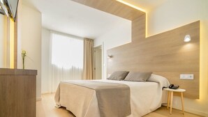 A modern bedroom with a wooden headboard, a bedside table with a lamp, and a bed with a beige bedspread. - Hotel Carlos l (Benidorm)