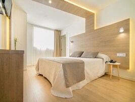 A modern bedroom with a wooden headboard, a bedside table with a lamp, and a bed with a beige bedspread.