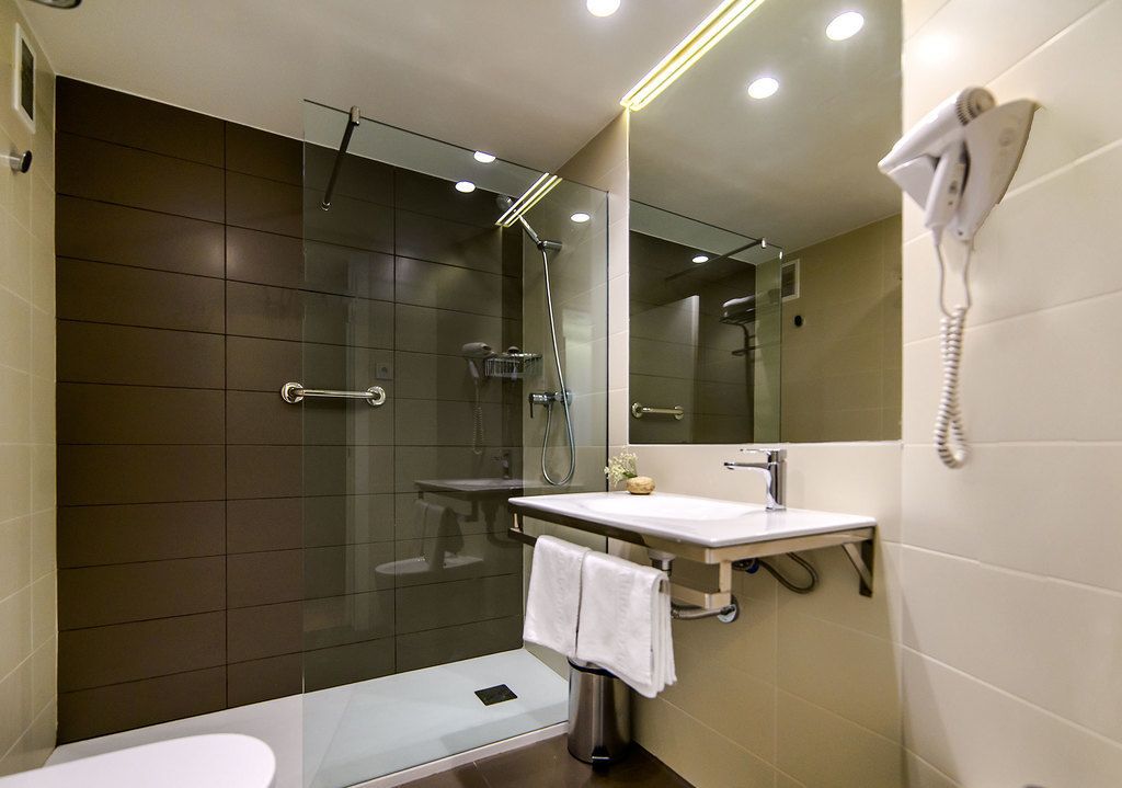 A modern bathroom with a glass-enclosed shower, a white sink, and a hairdryer mounted on the wall.