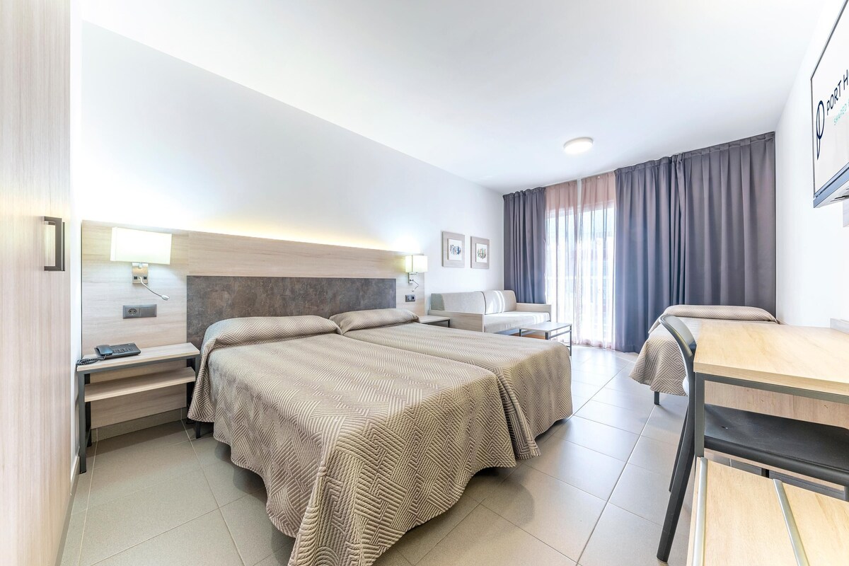 A hotel room with two beds, a desk, a chair, a lamp, and a window with curtains.