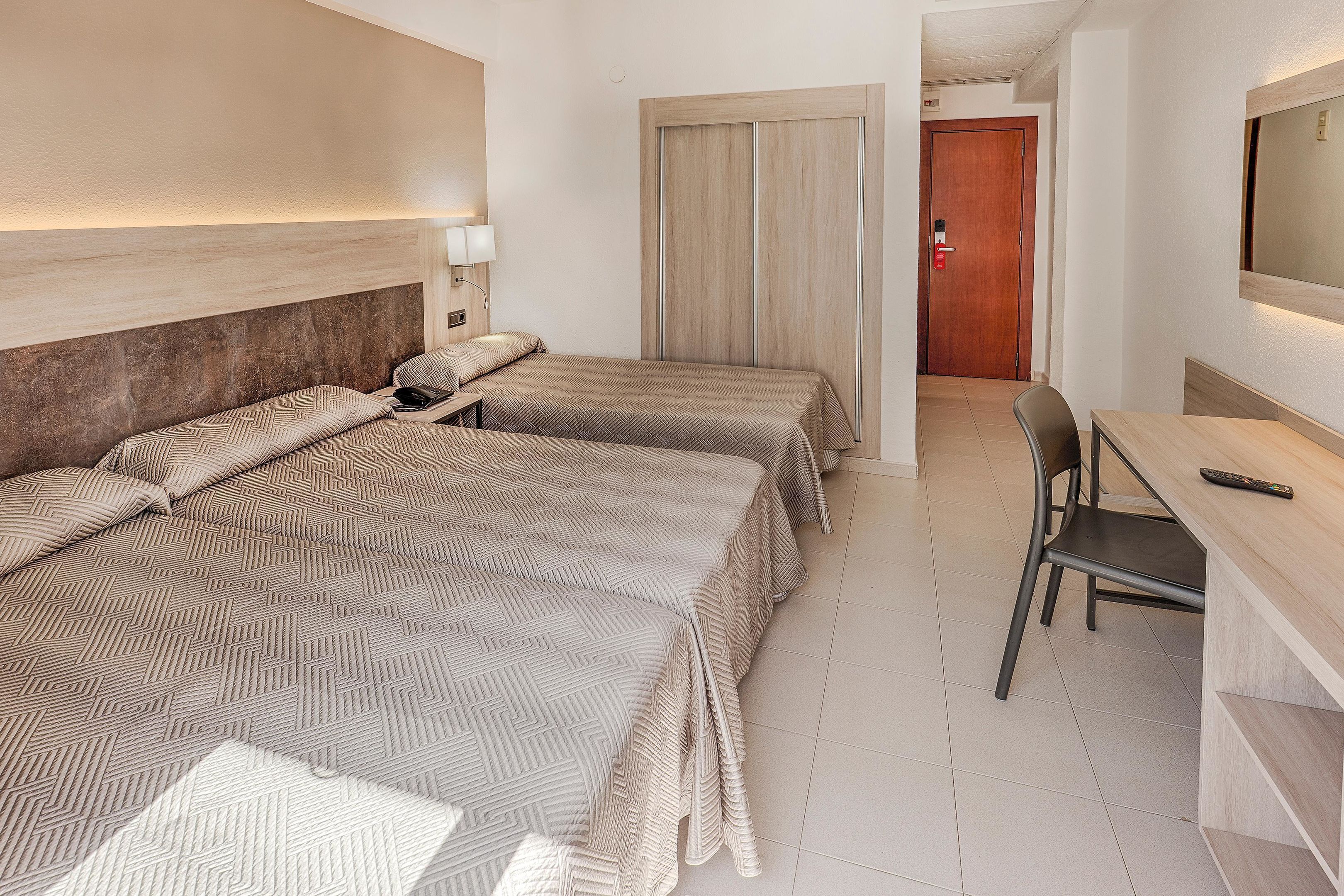 A hotel room with two beds, a desk, a chair, a TV, and a door.