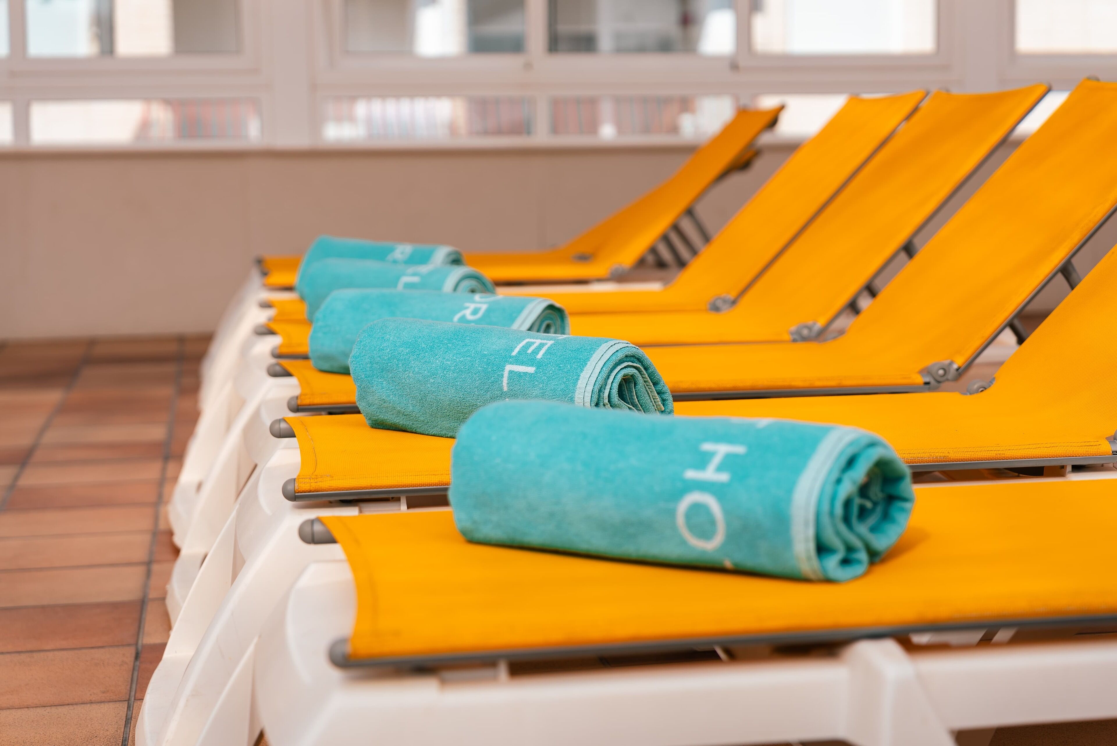 A row of sun loungers with towels rolled up, each with a visible letter on the towel.
