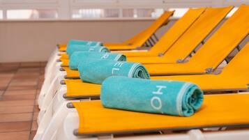 A row of sun loungers with towels rolled up, each with a visible letter on the towel.