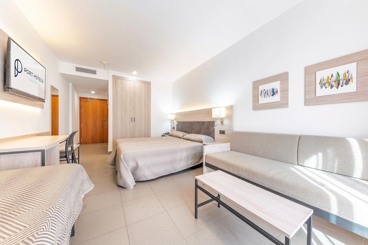 A modern hotel room with a bed, a sofa, a desk, and a chair. There is a sign on the wall and artwork on the wall.