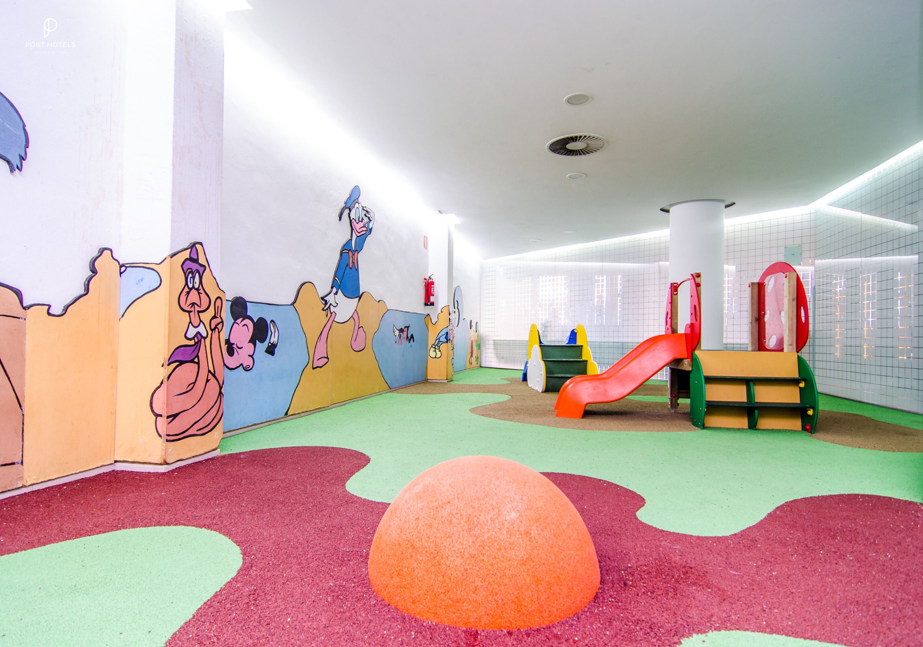 Un área de juegos infantiles con murales coloridos, un tobogán y suelo acolchado.