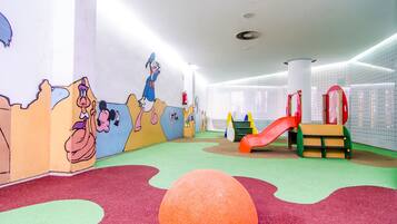 Un área de juegos infantiles con murales coloridos, un tobogán y suelo acolchado.